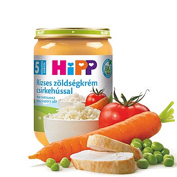 Egy üveg Hipp bébiétel idegen nyelvű címkével, körülötte friss hozzávalókkal, például rizzsel, sárgarépával, paradicsommal, borsóval és csirkével.
