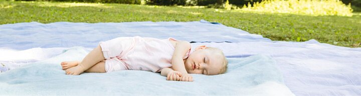 Egy kisbaba fekszik egy takarón egy füves területen.
