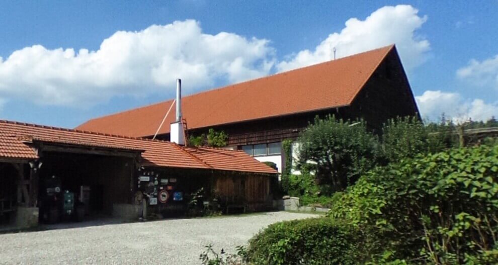 A building with a red roof and a chimney is surrounded by greenery under a blue sky with white clouds.