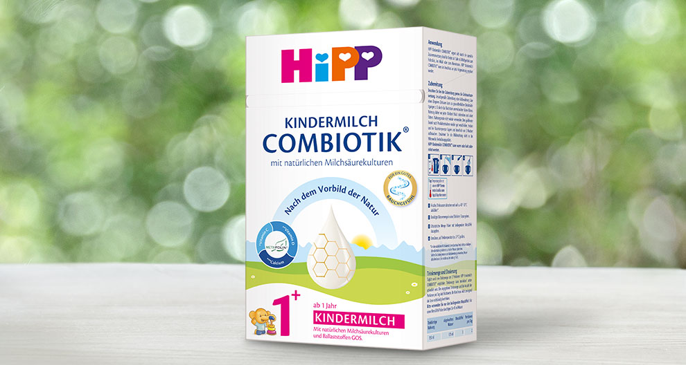 A white box with colorful text and graphics displays a product named "Kindermilch Combiotik," intended for children aged 1 and above, with a honeycomb graphic and a small cartoon bear.