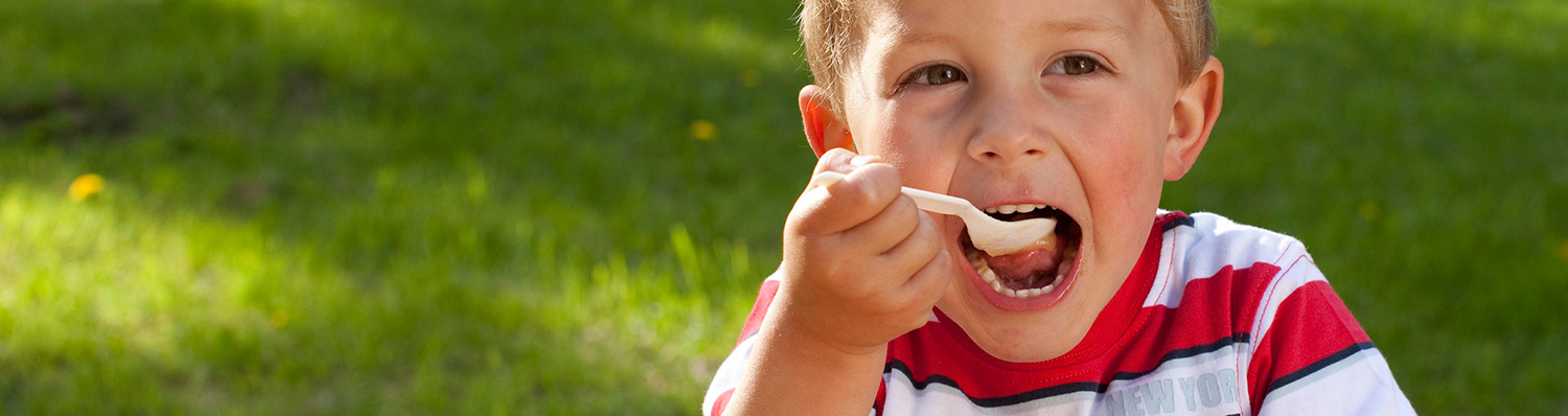 Egy kisgyermek a szabadban kanállal eszik.