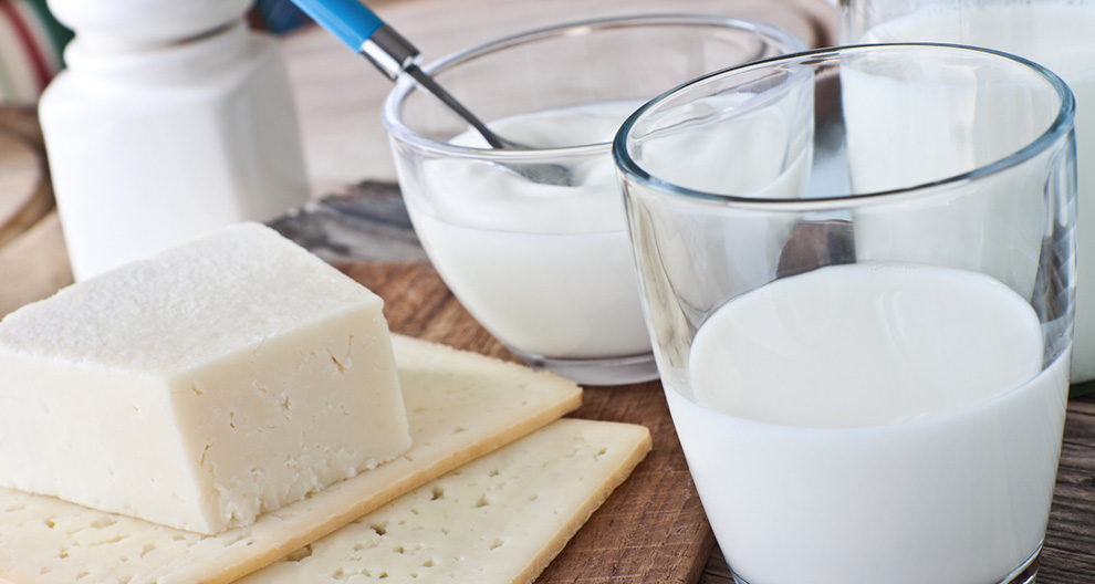 Egy pohár tej, egy tál joghurt, sajt és keksz egy faasztalon.