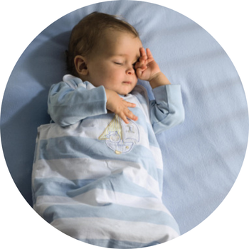 Egy baba fekszik egy kék lepedőn, csíkos, vitorlás mintás ruhát visel.