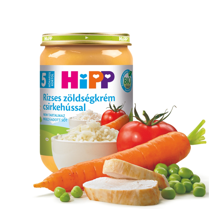 Egy üveg Hipp bébiétel idegen nyelvű címkével, körülötte friss hozzávalókkal, például rizzsel, sárgarépával, paradicsommal, borsóval és csirkével.